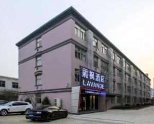 杭州Lavande Hotels·Hangzhou Xiaoshan International Airport的一座粉红色的建筑,前面有一辆汽车