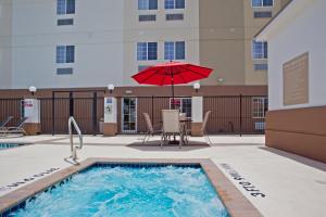 休斯顿Candlewood Suites Houston Westchase - Westheimer, an IHG Hotel的一个带红色遮阳伞和桌椅的游泳池