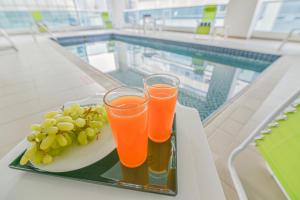 迪拜VISTA HOTEL APARTMENTS DELUXE的两杯橙汁和葡萄放在泳池旁的托盘上