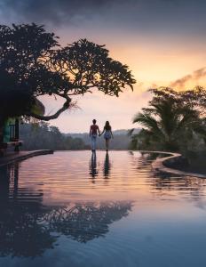 帕洋安阿迪瓦纳达拉阿尤别墅度假村的一对夫妇站在水面上,在日落前