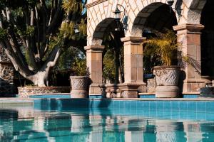 Villa del PueblitoHotel Ex Hacienda La Pitaya Querétaro的一座带拱门的建筑前的游泳池