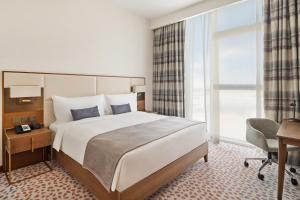 迪拜Staybridge Suites Dubai Al-Maktoum Airport, an IHG Hotel的酒店客房设有一张大床、一张桌子和一把椅子。