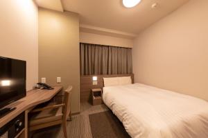 福井Dormy Inn Premium Fukui Natural Hot Spring的一间卧室配有一张床、一张书桌和一台电视