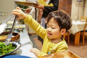 静冈Hotel Dorf Shizuoka的坐在餐桌前准备食物的男孩