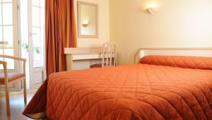 阿斯帕朗Relais Des Tilleuls的一间卧室配有一张带橙色床罩的床和一张书桌