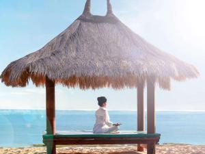 龙目岛库塔龙目岛诺富特度假别墅据点的坐在海滩上稻草伞下长凳上的人