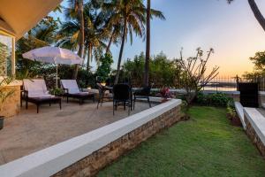 孟买amã Stays & Trails, Beach House Madh Island的庭院配有椅子和桌子及遮阳伞