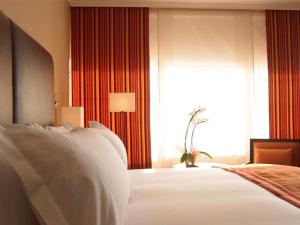 马德里铂尔曼马德里机场展会酒店的卧室配有白色床单、窗户和床。