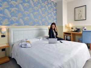雷焦艾米利亚雷焦艾米利亚美居阿斯托利亚中心酒店的坐在床上的女人在手机上讲话