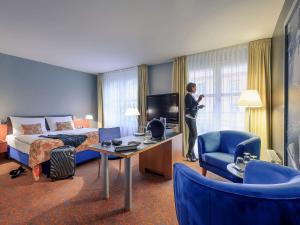 柏林美居酒店柏灵查勒边检站店的站在酒店房间的人,有一张床和电视