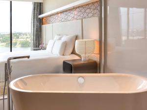 阿比让普尔曼阿比让酒店的卧室前的浴缸,卧室配有一张床