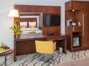 迪拜迪拜阿尔巴沙诺富特酒店的一间卧室配有一张床和一张书桌及电视