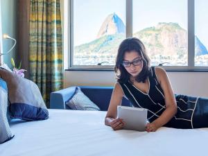 里约热内卢诺富特RJ普莱雅波塔佛歌酒店的坐在床上的女人,用平板电脑