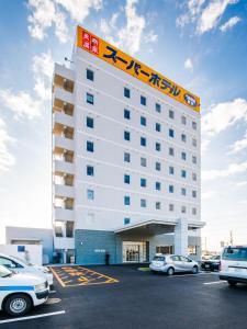 神栖市Super Hotel Kashima的停车场内停放汽车的酒店大楼