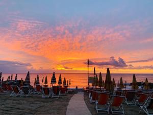 阿尔本加Piccolo Paradiso的日落时分海滩上的一组椅子和遮阳伞
