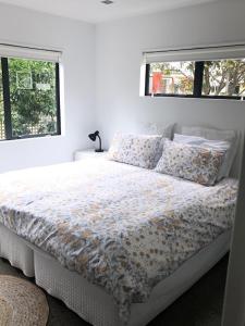 哈海Hahei Beach Apartment的白色卧室配有一张带花卉床罩的床和2个窗户