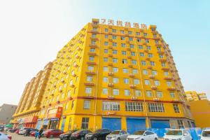 临汾7天优品·临汾平阳南街店的一座黄色的建筑,汽车停在停车场