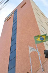 瓜拉廷格塔Lotus Hotel - à 6 km do Santuário de Aparecida-SP的前面有两面旗帜的高高的砖砌建筑