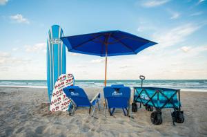 可可比奇Beachside Hotel and Suites的海滩上的2把蓝色椅子和1把遮阳伞