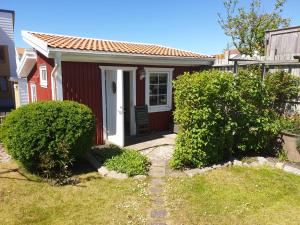 斯默根Stuga smögen的一间红色的房子,有一扇白色的门和两丛灌木