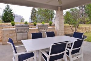 奥斯汀Candlewood Suites - Austin Airport, an IHG Hotel的露台上的白色桌椅,配有烧烤架