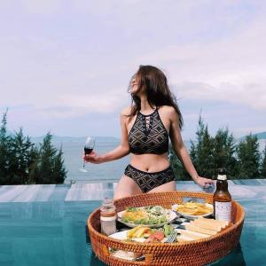 岘港Santori Hotel Da Nang Bay的一位穿着比基尼的女人,拿着一杯葡萄酒和一盘食物