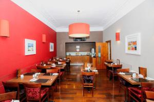 格拉斯哥Kelvingrove Hotel - Sauchiehall St的用餐室设有木桌和红色墙壁