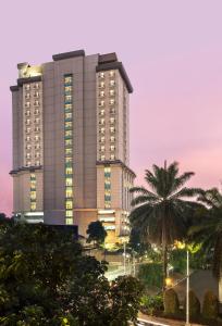 茂物Swiss-Belhotel Bogor的一座高大的建筑,前面有一棵棕榈树