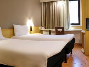 桑托斯ibis Santos Gonzaga Praia的酒店客房设有两张床和一张桌子。