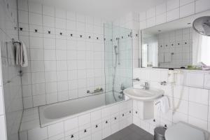 韦吉斯阿姆西美岸中央酒店的白色瓷砖浴室设有浴缸和水槽