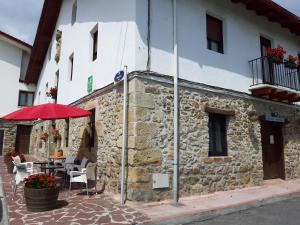 圣塞瓦斯蒂安Casa Rural Irigoien的一座石头建筑,配有红色的雨伞和一张桌子