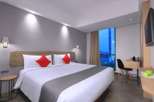 雅加达Neo Hotel Puri Indah的酒店客房配有一张带红色枕头的大型白色床。