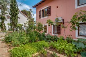 木洛希尼Apartments Villa Julija的粉红色房子前面的花园