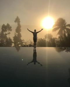 康提Aarunya Nature Resort and Spa的站在水面上,背着太阳的人