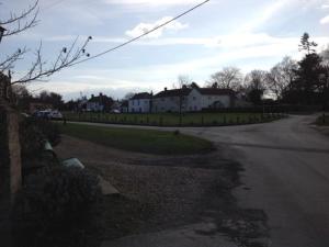 Shouldham ThorpeChalk and Cheese的一条空的街道,后面有房子,还有一条有汽车的道路