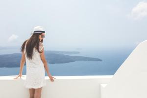 易莫洛林Agave Santorini Design Boutique Hotel的穿着白色衣服和帽子的女人,看着水面