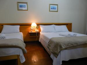 瓦尔任阿HOTEL VARGINHA的酒店客房设有两张床和一张带台灯的桌子。