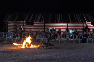 Al KhuraybahWadi Ghwere Camp مخيم وادي الغوير的一群人坐在海滩上的火堆旁
