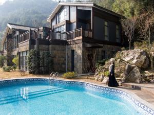 张家界张家界禾田居度假酒店的站在带游泳池的房子前面的女人