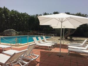 锡拉库扎Resort Villa Isola B&B的一组椅子和一把遮阳伞,位于游泳池旁