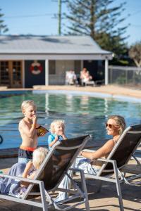 杰林冈维力海滩假日公园酒店的一名妇女和两名儿童坐在游泳池旁的草坪椅上
