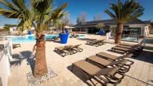 Langrune-sur-MerM&V Resort Camping的一组躺椅和棕榈树,毗邻一个游泳池