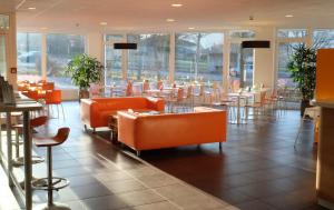 柯尼希斯温特ibis budget Hotel BONN SÜD Königswinter的餐厅设有橙色椅子和桌子以及窗户。