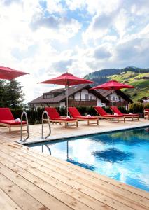 塞尔瓦迪加尔代纳山谷蒂罗尔酒店的一个带红色椅子和遮阳伞的度假游泳池