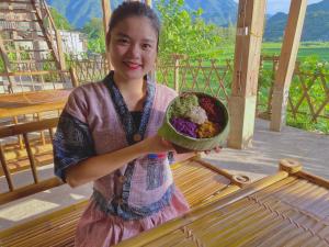 枚州县Meadow Mai Chau Homestay的拿着一碗食物的年轻女孩