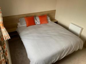 波斯考尔Caravan Porthcawl的一张大白色的床,上面有两个橙色枕头