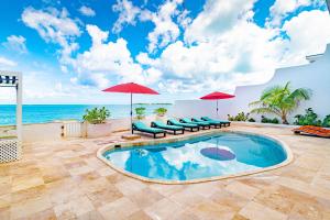 拿骚Caprice 7 -Oceanfront Villa - Gated Community with Pool的一个带椅子和遮阳伞的游泳池以及大海