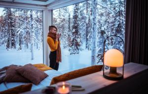 阿卡斯洛姆波罗Arctic Skylight Lodge的一位妇女通过窗户拍摄雪覆盖的森林