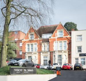 索利赫尔voco St. Johns Solihull, an IHG Hotel的一座砖砌建筑,前面有汽车停放