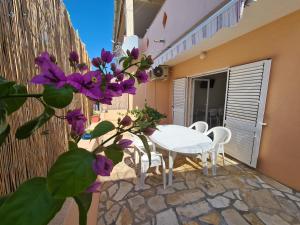 库斯提奇Apartments Barbati的庭院配有白色的桌椅和紫色的鲜花